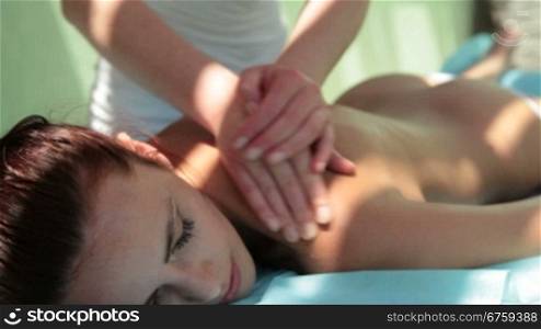 Beautiful woman outdoor receiving a back massage at spa resort.