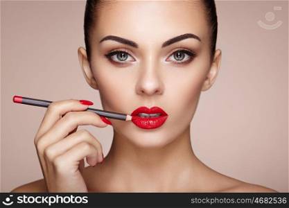 Beautiful woman paints lips with lipstick. Beautiful woman face. Makeup detail. Beauty girl with perfect skin. Red lips and nails manicure