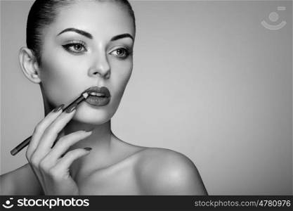 Beautiful woman paints lips with lipstick. Beautiful woman face. Makeup detail. Beauty girl with perfect skin. Red lips and nails manicure. Black and White