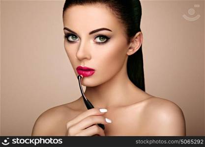 Beautiful woman paints lips with lipstick. Beautiful woman face. Makeup detail. Beauty girl with perfect skin. Red lips and nails manicure