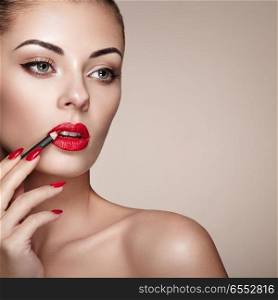 Beautiful Woman paints Lips with Lipstick. Beautiful Woman Face. Makeup detail. Beauty Model with Perfect Skin. Red Lips and Nails Manicure