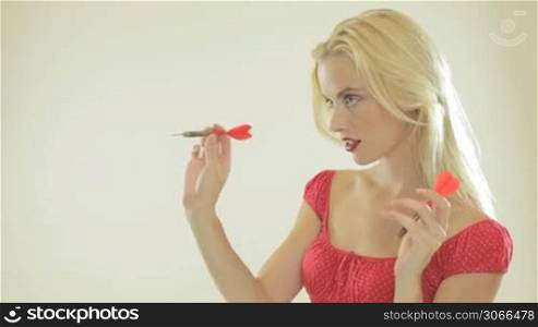 Beautiful woman playing darts concentrating as she takes aim, studio portrait with copyspace