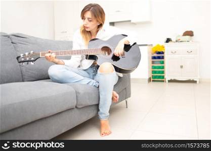 Beautiful woman plays her guitar on the sofa at home after work in the office.