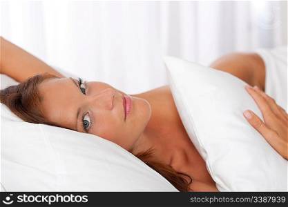 Beautiful woman posing in white bed, looking at camera
