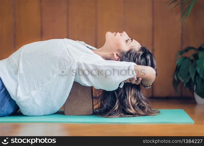 Beautiful woman practicing yoga using yoga blocks at home. Lying on back on turquoise yoga mat.