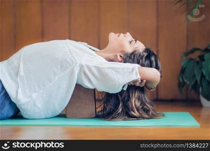 Beautiful woman practicing yoga using yoga blocks at home. Lying on back on turquoise yoga mat.