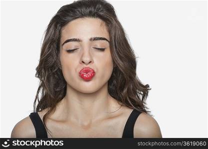 Beautiful woman puckering lips with eyes closed over gray background