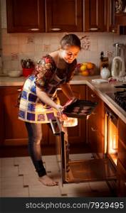 Beautiful woman putting chocolate cookies in hot oven