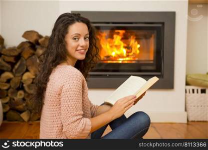 Beautiful woman reading a book at the warmth of the fireplace