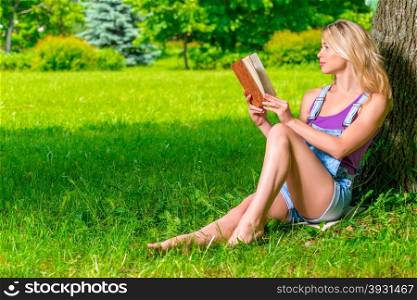 beautiful woman reading a romance sitting near a tree