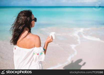 Beautiful woman relax during exotic vacation on the beach enjoying sweet coffee. Young woman with cup of hot coffee enjoy holidays