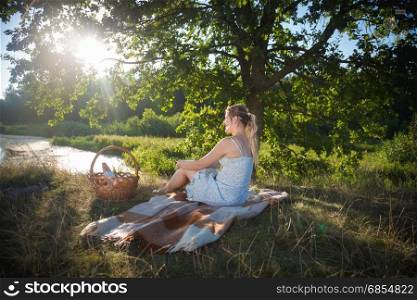 Beautiful woman relaxing on blanket under tree and looking at sunset