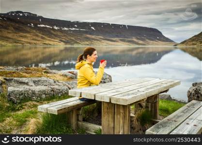 Beautiful woman resting close to a beautiful lake and drinkign a tea