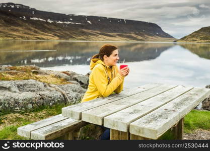 Beautiful woman resting close to a beautiful lake and drinkign a tea