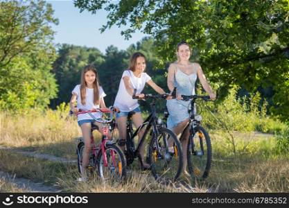 Beautiful woman riding with daughters on bicycles at field