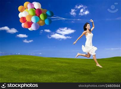 Beautiful woman running and jumping on a green meadow with a colored ballons