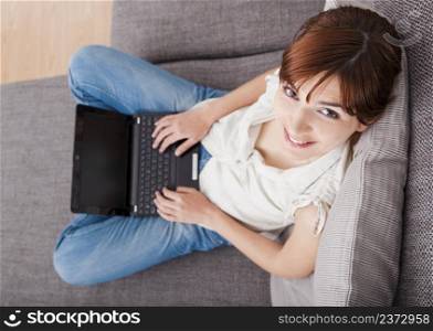 Beautiful woman seated on sofa and working with a laptop