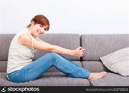 Beautiful woman seated on sofa holding a cellphone and sending a sms