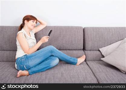 Beautiful woman seated on sofa holding a cellphone and sending a sms