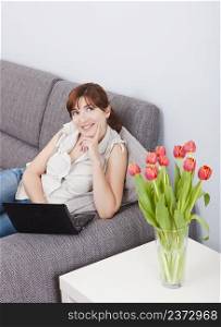Beautiful woman seated on sofa with a laptop and thinking on something