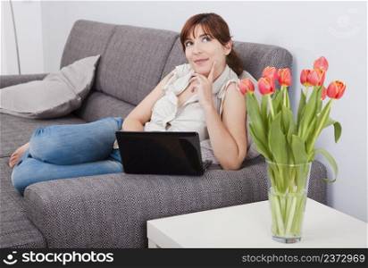 Beautiful woman seated on sofa with a laptop and thinking on something