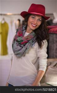 Beautiful woman shopping in clothing store standing near shelf and wearing red hat