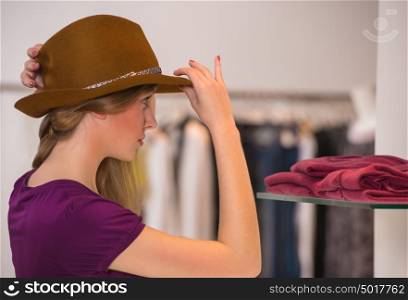 Beautiful woman shopping in clothing store trying on brown hat in front of mirror
