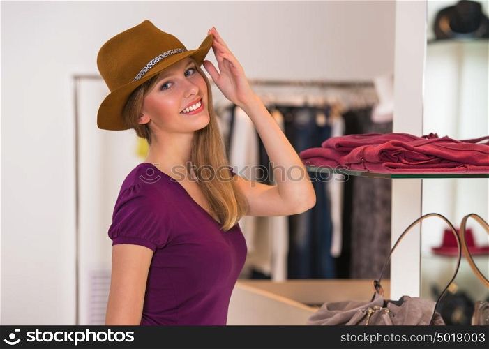 Beautiful woman shopping in clothing store wearing brown hat and looking at camera