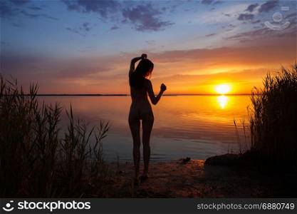 Beautiful woman silhouette at the ocean coast over sunset sky
