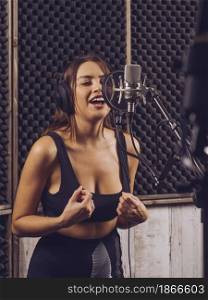 Beautiful woman singing into a large diaphragm microphone in a professional recording studio.