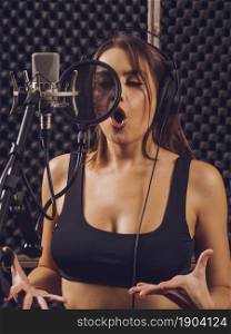 Beautiful woman singing into a large diaphragm microphone in a professional recording studio.