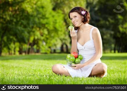 Beautiful woman sits and eats an apple on lawn, horizontally