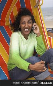 Beautiful woman sitting in a beachchair on a windy day and laughing on the phone