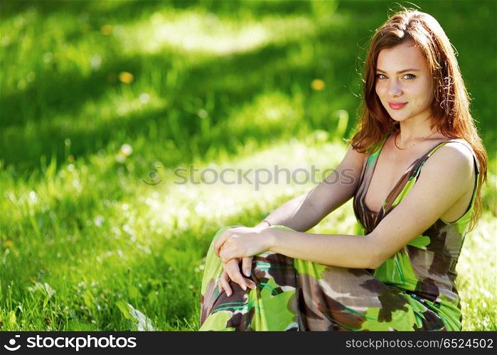 Beautiful woman sitting in a green field enjoying the summer sunlight. Woman sitting in a green field