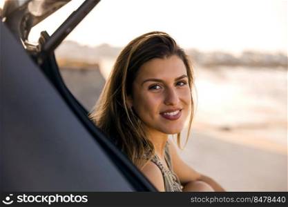 Beautiful woman sitting in the trunk of a car near a beach and smilling