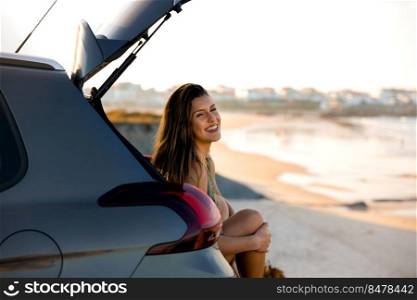 Beautiful woman sitting in the trunk of a car near a beach and smilling