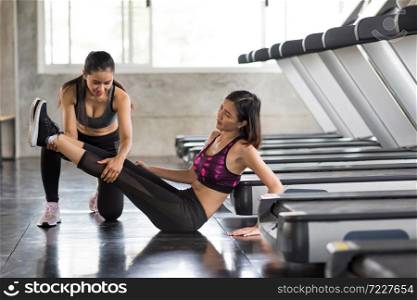 beautiful woman sitting near electric treadmill,her leg hurt from exercise while her friend or trainer try to first aid at fitness gym. Healthy lifestyle and health care insurance concept.