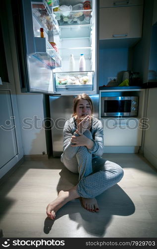 Beautiful woman sitting near refrigerator at late night