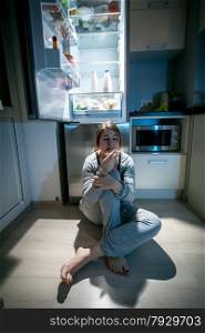 Beautiful woman sitting near refrigerator at late night