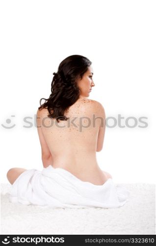 Beautiful woman sitting nude on soft surface with a towel around her bottom showing bare back with freckles, isolated.