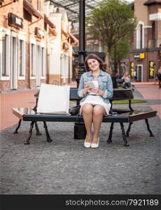 Beautiful woman sitting on bench with shopping bags and using tablet