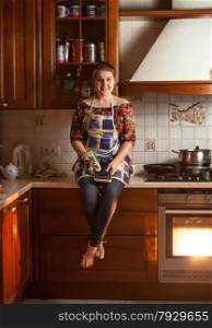 Beautiful woman sitting on tabletop while cooking dinner in oven