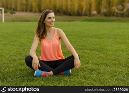 Beautiful woman sitting on the grass and relaxing after exercise