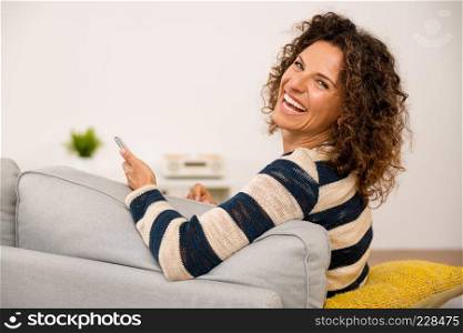 Beautiful woman sitting on the sofa and laughing while sending a text message