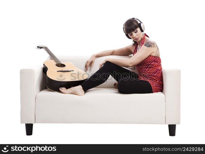 Beautiful woman sitting on the sofa with her guitar and listen music, isolated on white