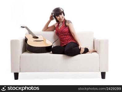 Beautiful woman sitting on the sofa with her guitar and listen music, isolated on white