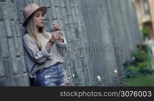 Beautiful woman smoking and leaning on the loft brick wall. Sexy blonde female smoking under stress and wanting to relax, letting out smoke cigarettes