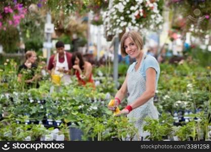 Beautiful woman spraying water on plants with people in background