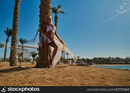 beautiful woman standing near the palm tree on the beach.. beautiful woman standing near the palm tree on the beach