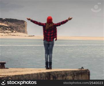 Beautiful woman standing on a pier with arms raised feeling the freedom
